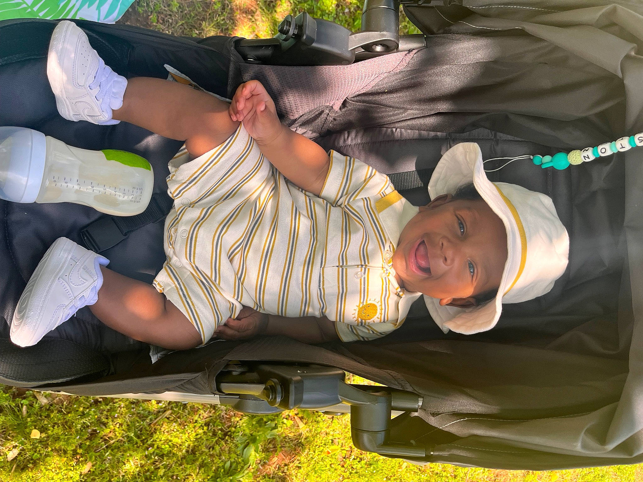 Houston is registered to the contest to win money with this photo: baby, child, comfort, elbow, fun, grass, green, hat, headwear, human_leg, knee, lap, leisure, person, plant, shorts, smile, t_shirt, thigh, toddler