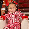 child, girl, pajamas, red_bows, armchair, christmas_presents, holiday, wreath, smiling, festive, indoor, decorations, winter, snowflakes, cozy, portrait, cute, holiday_season, celebration, happy