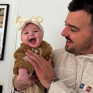 Haylee participe au concours pour gagner de l'argent avec cette photo : baby, infant, smiling, laughing, bow_headband, father, man, holding_baby, hoodie, watch, ring, door, picture_frame, indoor, cozy_clothing, knit_texture, portrait, toes, hand, person