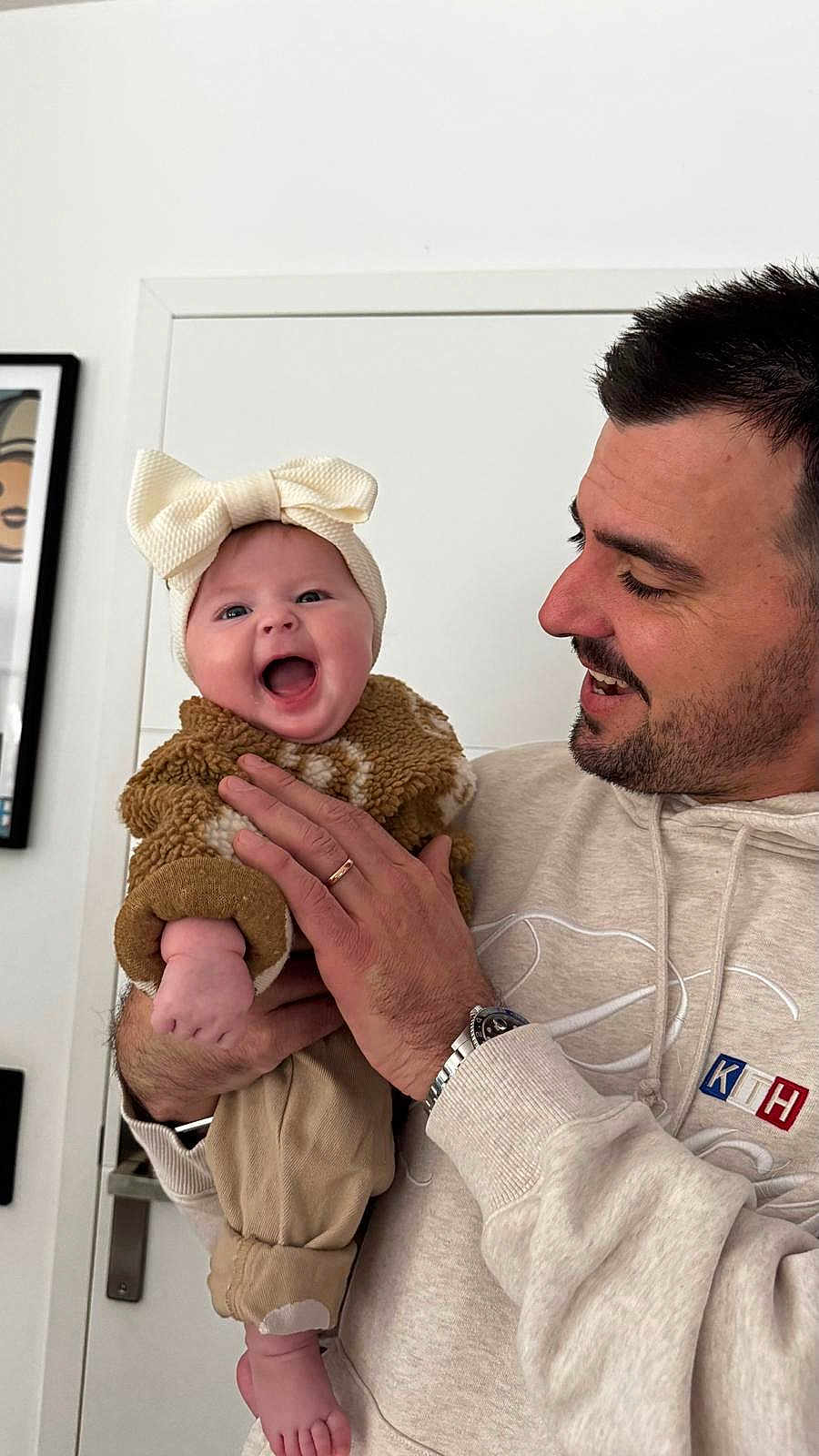 Haylee participe au concours pour gagner de l'argent avec cette photo : baby, infant, smiling, laughing, bow_headband, father, man, holding_baby, hoodie, watch, ring, door, picture_frame, indoor, cozy_clothing, knit_texture, portrait, toes, hand, person