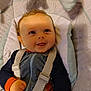 baby, baby_seat, child, closeup, curly_hair, cushion, cute, face, happy, indoor, infant, looking_up, orange_sleeves, pajamas, portrait, seat_belt, small_hand, smiling, soft_toy, striped_clothing
