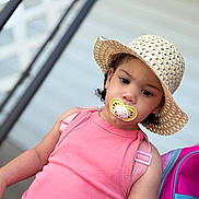 Génesis joined the competition — help win amazing prizes! toddler, child, pacifier, hat, pink_top, backpack, outdoor, portrait, person, curly_hair, expression, sitting, railing, casual, summer, young_child, fashion, closeup, headwear, daylight