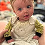 William is registered to the contest to win money with this photo: baby, child, infant, face, eyes, onesie, clothing, hand, person, cute, expression, indoor, blurred, holding, soft_toys, people, skin, head, hair, background