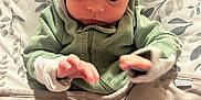 William is registered to the contest to win money with this photo: baby, child, green_hoodie, blanket, cushion, seat, shadow, hand, curious, infant, indoor, person, clothing, fabric, head, face, young, sitting, looking_down, home