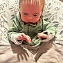 baby, child, green_hoodie, blanket, cushion, seat, shadow, hand, curious, infant, indoor, person, clothing, fabric, head, face, young, sitting, looking_down, home