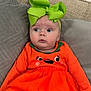 Sylvia is registered to the contest to win money with this photo: baby, child, infant, orange_dress, green_bow, couch, pillow, face, wide_eyes, cute, indoors, seated, clothing, tights, expression, headwear, holiday_theme, soft_furniture, portrait, young_child