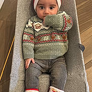 Gabriel participe au concours pour gagner de l'argent avec cette photo : baby, child, infant, santa_hat, christmas_sweater, socks, baby_seat, indoors, flooring, cozy, holiday, festive, cute, thumb_sucking, clothing, person, smiling, winter_wear, seated, headwear