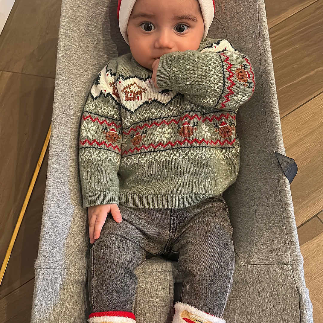 Gabriel participe au concours pour gagner de l'argent avec cette photo : baby, baby_seat, child, christmas_sweater, clothing, cozy, cute, festive, flooring, headwear, holiday, indoors, infant, person, santa_hat, seated, smiling, socks, thumb_sucking, winter_wear