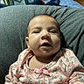 Maylynn is registered to the contest to win money with this photo: baby, infant, child, face, portrait, sitting, indoors, floral_outfit, pink_clothing, bow, smiling, curious, open_mouth, gray_blanket, lap, bedroom, bed, furniture, close_up, home