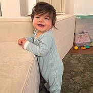 Aslan participe au concours pour gagner de l'argent avec cette photo : baby, child, onesie, standing, smiling, hair, couch, living_room, carpet, toy, plastic_box, floor, furniture, happy, indoor, person, cute, infant, home, play