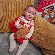 Echo is registered to the contest to win money with this photo: baby, child, clothing, couch, cozy, cute, face, festive, gingerbread_house, happy, holiday, home, indoor, infant, pillow, plush, red_skirt, smiling, tights, toy
