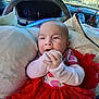 baby, infant, child, car_interior, red_dress, tutu, cushion, dashboard, steering_wheel, hands, curious_expression, seat, window, sunlight, clothing, person, portrait, indoor, seatbelt, car
