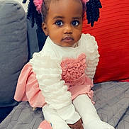 Angélique a rejoint le concours — aidez-le/la à gagner de superbes lots ! toddler, child, girl, pink, hair_accessories, dress, white_tights, toy, blanket, couch, cushion, indoor, portrait, cute, seated, curly_hair, expression, soft_toy, cozy, colorful