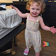Paisley is registered to the contest to win money with this photo: toddler, child, indoor, wooden_floor, pink_slippers, curly_hair, smiling, dress, toy, bed, chair, lamp, mirror, furniture, room, playful, happy, person, casual, home