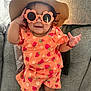 toddler, child, sunglasses, hat, orange_clothing, strawberry_pattern, smile, couch, indoor, happy, baby, bracelet, shorts, shirt, person, furniture, cute, playful, sunhat, glasses