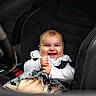 baby, smiling, car_seat, child, infant, clothing, lace, happy, portrait, seatbelt, car_interior, cute, sitting, young_child, person, black, white, fabric, cute_expression, indoor