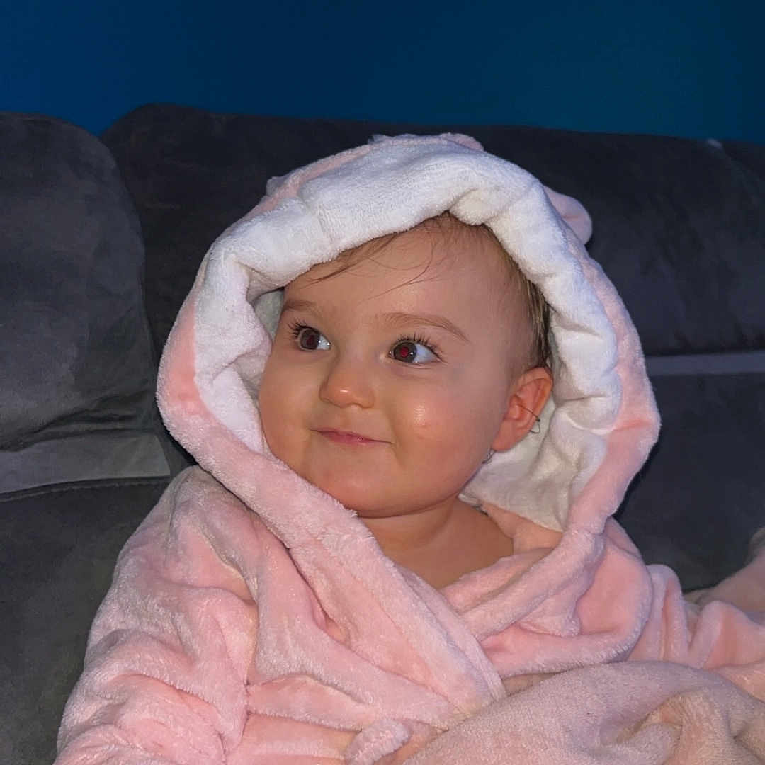 Victoria participe au concours pour gagner de l'argent avec cette photo : baby, child, pink_robe, blanket, sofa, indoor, smile, face, hood, cute, comfort, warm, portrait, young_child, person, cozy, expression, seated, soft_texture, home