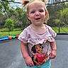 toddler, child, pigtails, smiling, trampoline, outdoor, basketball_hoop, greenery, shorts, shirt, cartoon_character, daylight, play, happy, nature, grass, trees, person, young_child, summer_clothing