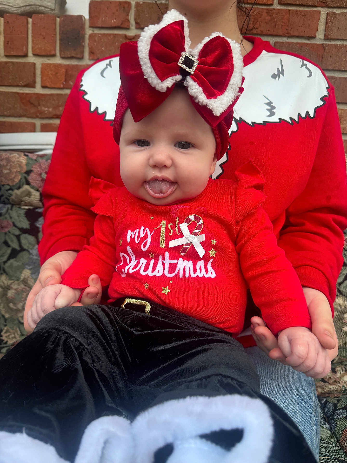 Kaliyah is registered to the contest to win money with this photo: baby, child, infant, red_clothing, christmas, holiday, headband, bow, tongue_out, holding_hands, adult, brick_wall, outdoor, festive, cute, smiling, person, celebration, winter, sitting