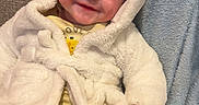 Noah joined the competition — help win amazing prizes! apparel, baby, blanket, child, couch, cozy, cute, face, happy, home, hoodie, indoor, infant, person, portrait, sitting, smiling, soft_texture, white_clothing, yellow_clothing
