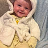 baby, child, smiling, hoodie, white_clothing, yellow_clothing, couch, blanket, indoor, cute, face, person, portrait, soft_texture, cozy, sitting, infant, happy, apparel, home