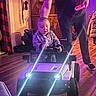 Payton is registered to the contest to win money with this photo: adult, cabinet, child, curtain, floor, furniture, headlights, home, indoor, jacket, lighting, person, person_holding, playful, remote_control, smiling, steering_wheel, toddler, toy_car, wooden_floor
