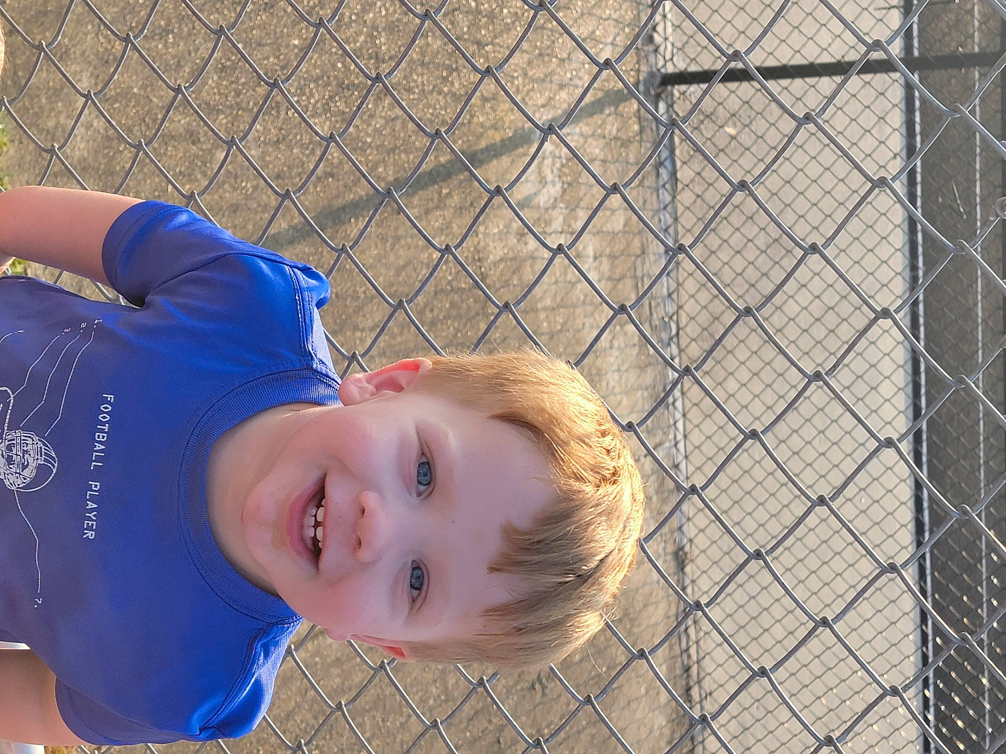 Walker is registered to the contest to win money with this photo: baseball_cap, chain_link_fencing, child, electric_blue, fence, fun, grass, happy, hat, joy, leisure, mammal, mesh, pattern, person, portrait_photography, recreation, smile, soil, toddler