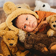 Richie is registered to the contest to win money with this photo: baby, infant, teddy_bear, stuffed_animal, plush_toy, hat, brown, orange, wooden_floor, cute, child, portrait, soft_texture, indoors, cozy, lying_down, closeup, adorable, warm_colors, baby_clothing