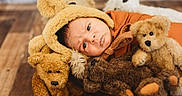 Richie is registered to the contest to win money with this photo: baby, infant, teddy_bear, stuffed_animal, plush_toy, hat, brown, orange, wooden_floor, cute, child, portrait, soft_texture, indoors, cozy, lying_down, closeup, adorable, warm_colors, baby_clothing
