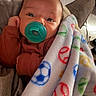 baby, pacifier, blanket, peace_sign, soccer_ball, pillow, couch, infant, clothing, face, hand, comfort, indoor, soft_texture, resting, cute, portrait, child, snuggle, warm