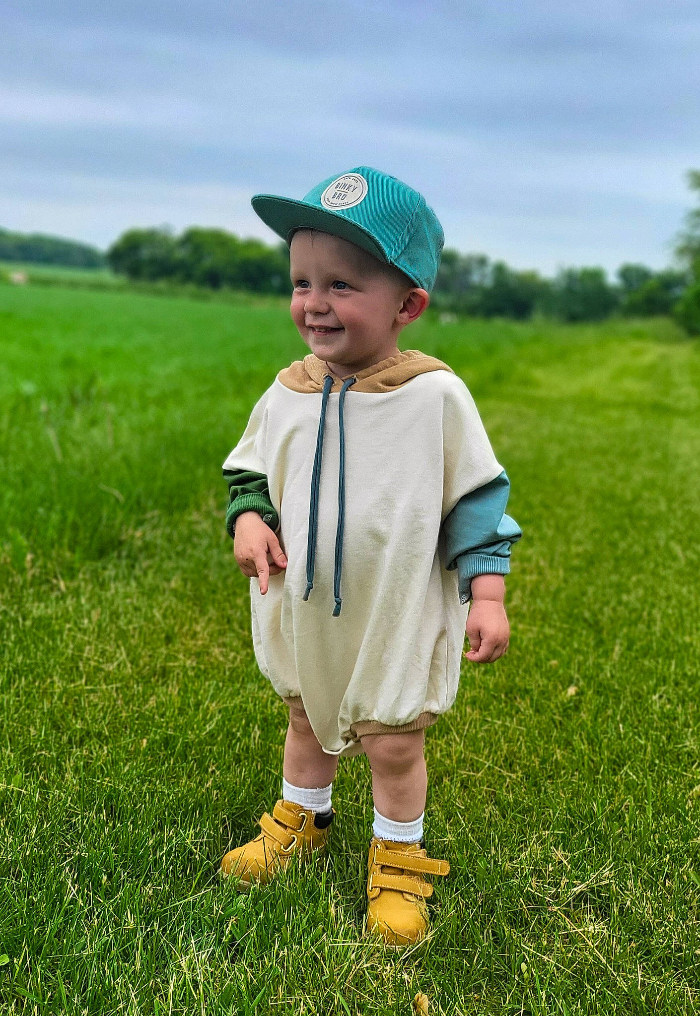 Finn is registered to the contest to win money with this photo: baby_toddler_clothing, baseball_cap, cap, cloud, fun, gesture, grass, grassland, happy, hat, headgear, headwear, joy, landscape, lawn, people_in_nature, person, plant, shorts, sky