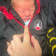 Brodie-Lee is registered to the contest to win money with this photo: newborn, baby, hand, jacket, zipper, black_clothing, red_clothing, person, infant, warm_clothing, face, holding, closeup, cute, portrait, young_child, indoor, soft_light, skin, clothing_logo
