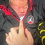 newborn, baby, hand, jacket, zipper, black_clothing, red_clothing, person, infant, warm_clothing, face, holding, closeup, cute, portrait, young_child, indoor, soft_light, skin, clothing_logo