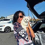 Vizzy joined the competition — help win amazing prizes! accessory, animal, blue_eyes, car, casual_clothing, cat, daytime, holding, open_trunk, outdoor, parking_lot, patterned_sweater, person, pet, road, sunglasses, sunny, transportation, white_cat, woman