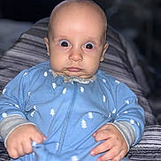 Colton is registered to the contest to win money with this photo: baby, infant, blue_onesie, hands, face, wide_eyes, expression, person, indoor, blanket, striped_blanket, clothing, child, portrait, sitting, cute, young, human, closeup, soft_lighting