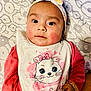 adorable, baby, bib, blanket, cartoon_cat, child, closeup, cute, expression, face, headband, indoors, infant, lying_down, pattern, person, pink_clothing, portrait, rosy_cheeks, small_hand
