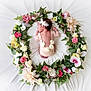 baby, newborn, flower_wreath, pink_lace, sleeping, headband, floral_arrangement, green_leaves, white_background, peaceful, infant, portrait, cute, decorative, soft_texture, delicate, resting, baby_clothing, nature, artistic