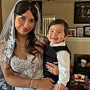 Luca is registered to the contest to win money with this photo: bride, wedding_dress, veil, child, toddler, smile, portrait, indoor, person, holding, happy, toy, living_room, furniture, photography, ring, phone, lace, clothing, family