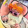 Alita is registered to the contest to win money with this photo: baby, infant, car_seat, headband, bow, sunglasses, bib, blanket, pink, orange, clothing, person, cute, child, seat, warning_label, hand, face, cozy, indoor