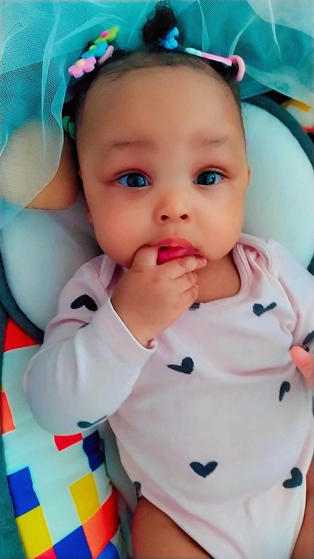 Diamond joined the competition — help win amazing prizes! baby, infant, child, face, hand, clothing, onesie, hair_clips, colorful, blanket, pattern, heart_pattern, soft, cute, indoors, portrait, lying_down, expression, curious, skin