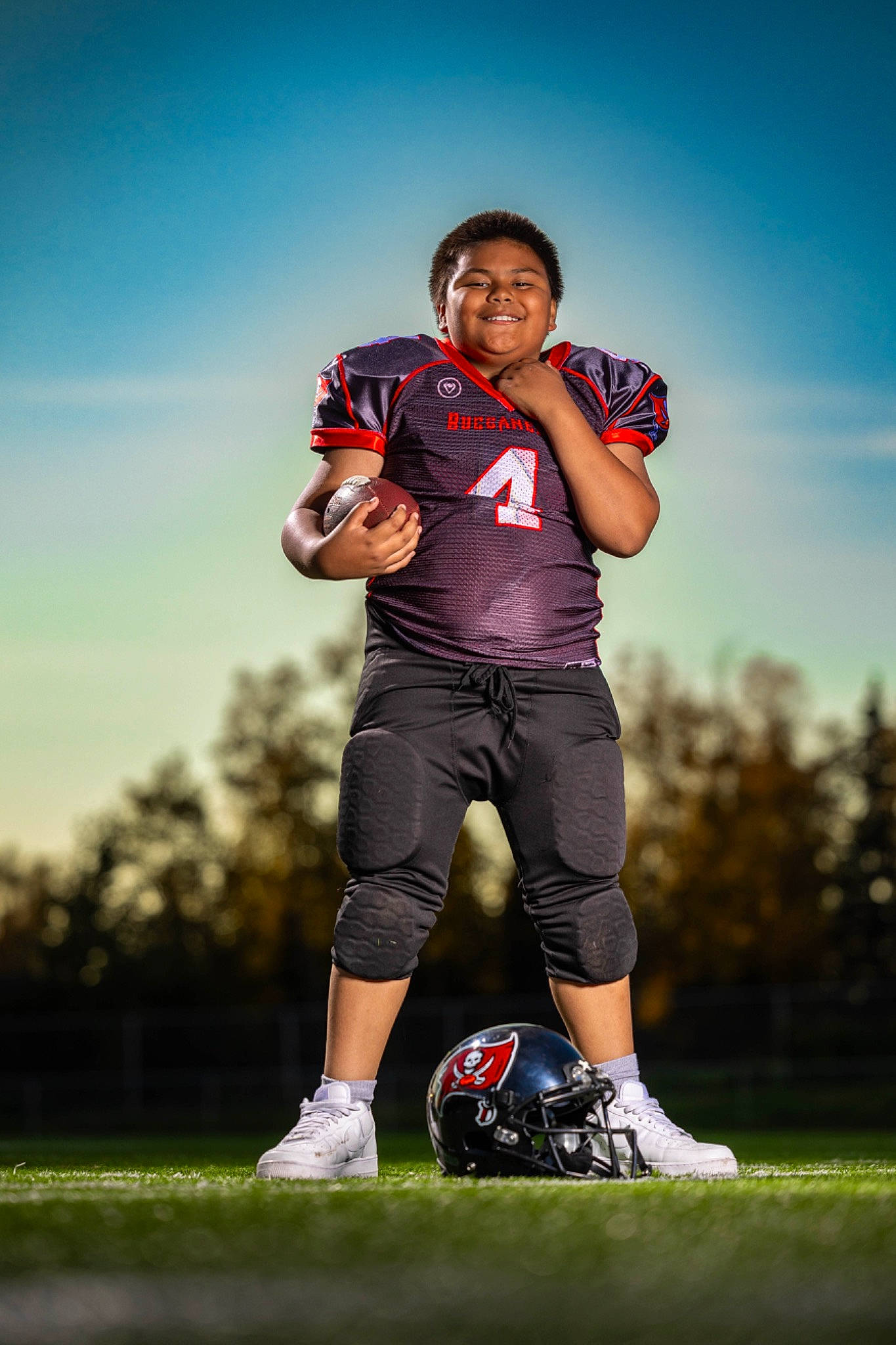 Aiden is registered to the contest to win money with this photo: ball, flash_photography, football, grass, grassland, happy, joy, knee, leisure, person, plant, player, recreation, shorts, sky, smile, sneakers, sports_equipment, sports_uniform, sportswear
