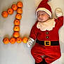 baby, sleeping, santa_claus_costume, tangerines, number_one, orange, infant, holiday, festive, cute, lying_down, soft_surface, gloves, hat, face, child, one, footwear, red_clothing, white_background