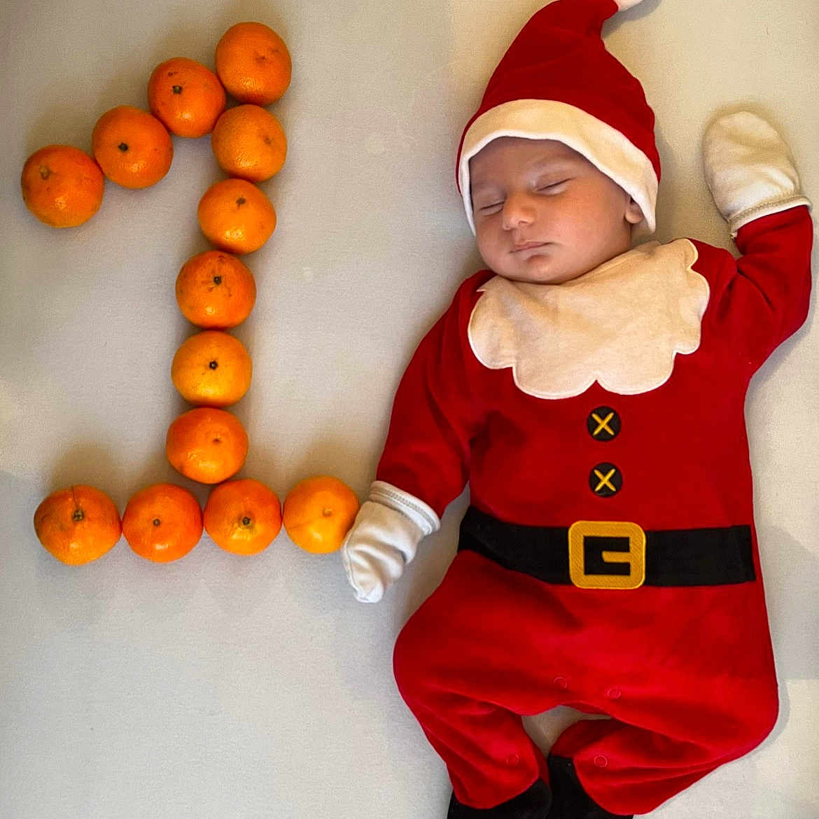 Serafin participe au concours pour gagner de l'argent avec cette photo : baby, child, cute, face, festive, footwear, gloves, hat, holiday, infant, lying_down, number_one, one, orange, red_clothing, santa_claus_costume, sleeping, soft_surface, tangerines, white_background