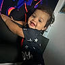 Dasean is registered to the contest to win money with this photo: toddler, child, smile, curly_hair, indoor, clothing, furniture, face, happy, portrait, person, black_background, art, colorful, pattern, star_pattern, young_child, cute, baby, holding