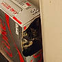 animal, beverage_packaging, cardboard_box, cat, closeup, container, curious, diet_coke, feline, hiding, household, indoor, mischievous, peeking, pet, tortoiseshell_cat, wall, whiskers, wooden_floor, yellow_eyes