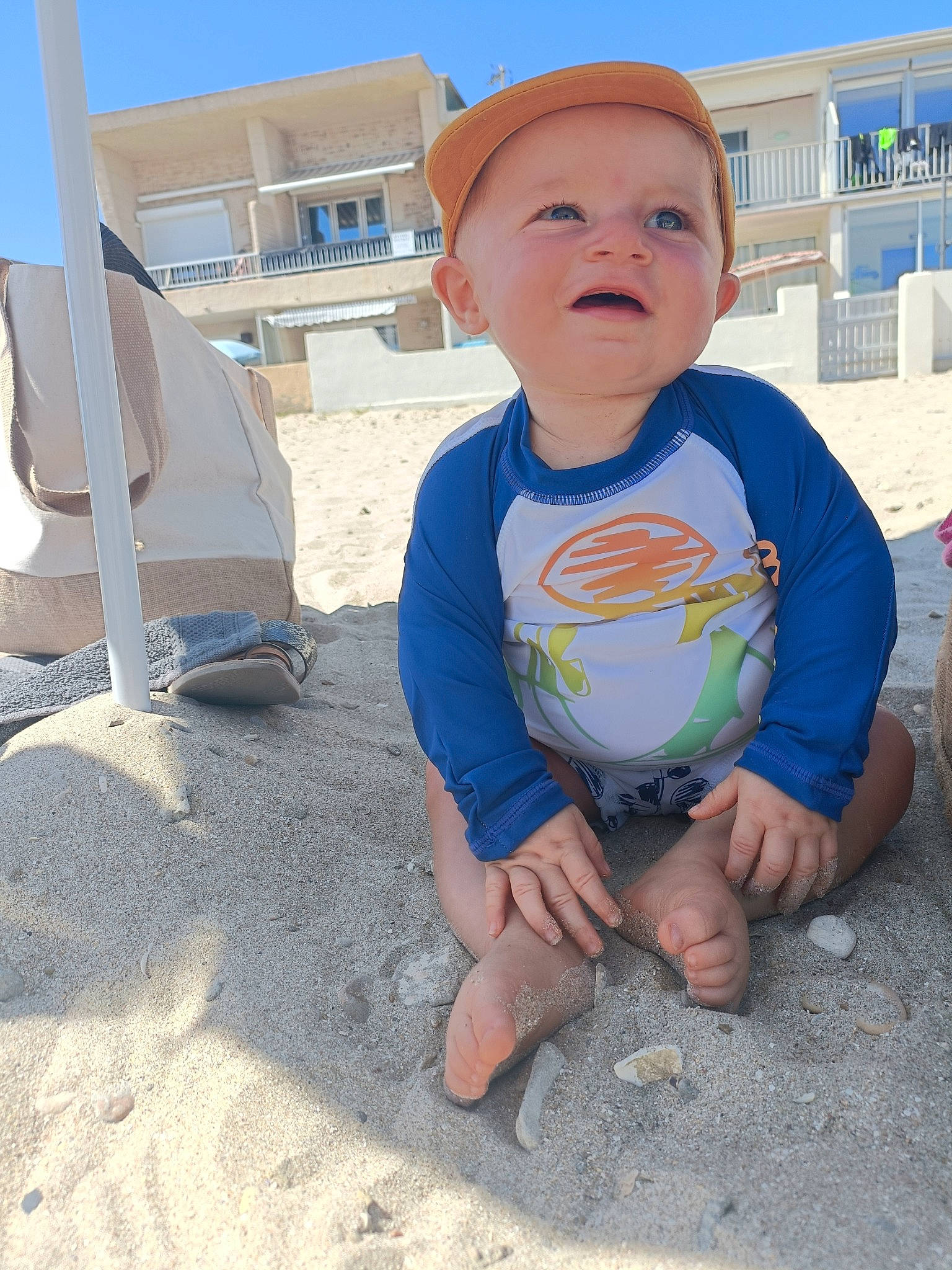 Liam participe au concours pour gagner de l'argent avec cette photo : azure, baby, baby_toddler_clothing, child, foot, fun, happy, hat, landscape, leisure, person, personal_protective_equipment, play, public_space, recreation, sand, sitting, sky, t_shirt, toddler
