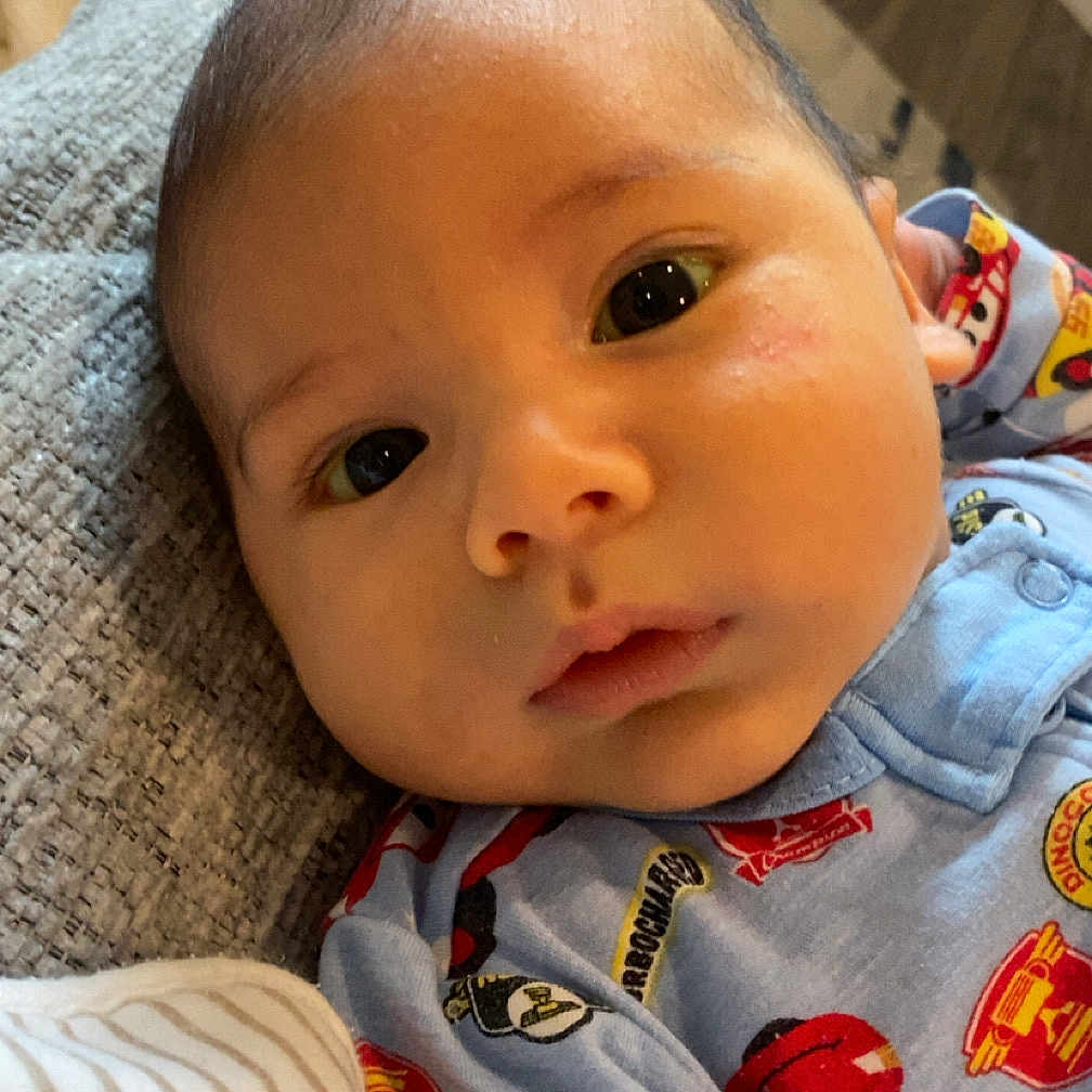 Alonso is registered to the contest to win money with this photo: baby, infant, child, portrait, close_up, face, eyes, wide_eyed, looking_at_camera, indoor, couch, pajamas, clothing, cartoon, colorful, cozy, home, sitting, photography, closeup