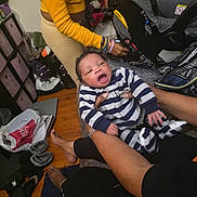 Kamarion Swinger joined the competition — help win amazing prizes! baby, infant, striped_onesie, yawning, car_seat, adult_hands, bracelets, yellow_sweater, slippers, hardwood_floor, rug, shopping_bag, diaper_bag, clutter, indoor, living_room, portrait, candid, family, person_holding_baby