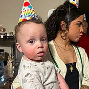 Jonah joined the competition — help win amazing prizes! background, birthday_hat, celebration, child, curly_hair, earrings, facial_expression, holding, indoor, jewelry, long_sleeve, necklace, party, people, portrait, rosy_cheeks, sweater, table, toddler, woman
