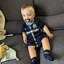 toddler, pacifier, child, blue_eyes, sports_jersey, socks, couch, toy, blanket, indoor, person, seated, beads, clothing, furniture, cute, comfort, home, portrait, young_child